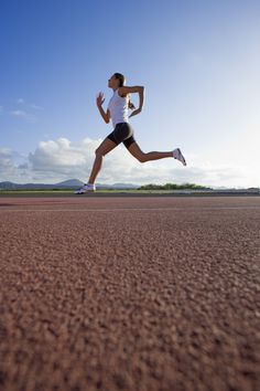 a woman running across a dirt field with the sun shining on her face and legs