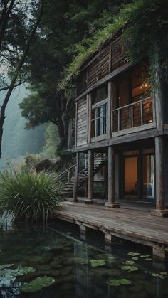 a wooden house sitting on top of a lush green forest next to a body of water