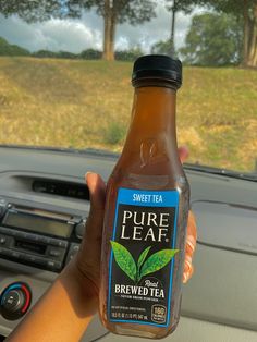a person holding up a bottle of pure leaf iced tea in their hand while driving
