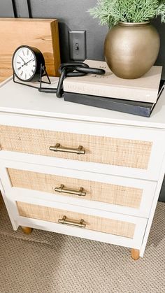 a white dresser with books and a clock on it next to a potted plant