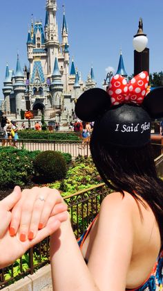 a woman wearing a minnie mouse hat in front of a castle
