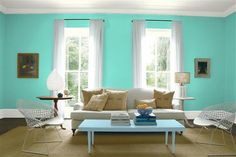 a living room with green walls, white furniture and two large windows in the corner