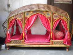 the bed is made out of wood and has pink sheets on it, with red drapes