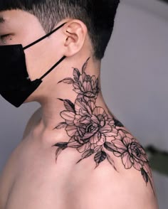 a man wearing a face mask with flowers on his neck and behind him is a black floral tattoo