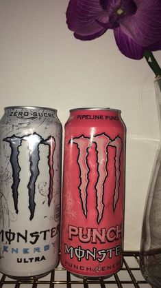 two cans of monster energy drink sitting on a shelf next to a vase with flowers