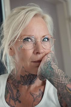 a woman with tattoos on her arms and chest is looking at the camera while holding her hand to her face