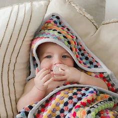 a baby wrapped up in a blanket with food in it's mouth while laying on a couch