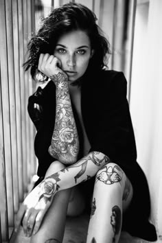 a woman sitting on the ground with tattoos on her arms and legs, looking at the camera