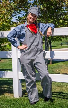 a woman standing in front of a white fence wearing overalls and a bandana