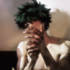 a man with green hair covers his face while sitting in front of a wall and holding his hands to his chest