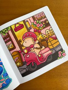 an open book on a wooden table with a drawing of a girl riding a scooter