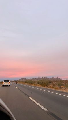 a car driving down the road with mountains in the background and pink skies above it