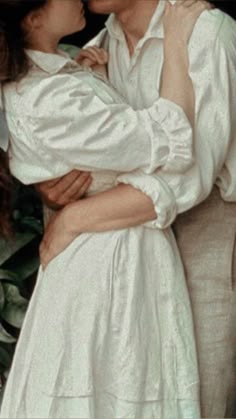 a man and woman kissing each other in front of a plant with green leaves behind them