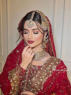 a woman wearing a red and gold bridal outfit with her hands on her chin