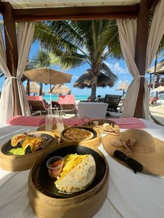 a table topped with plates of food next to an umbrella covered beach side chair and palm trees