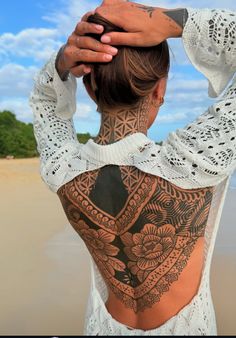 a woman with tattoos on her back standing in front of the ocean and holding her hands up to her head