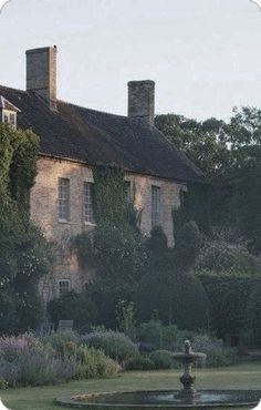 an old house with a fountain in the foreground and lots of trees around it