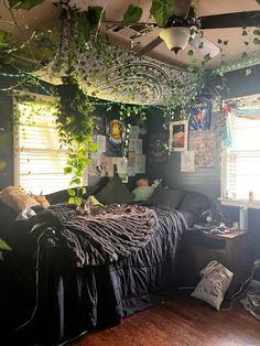 an unmade bed with lots of plants hanging from the ceiling