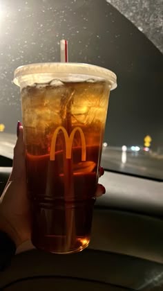 a person holding up a drink in the back seat of a car with a mcdonald's sign on it