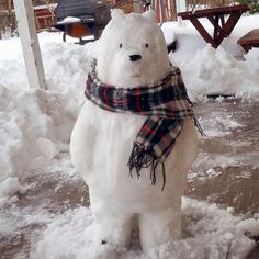 a large white polar bear standing in the snow with a scarf around it's neck