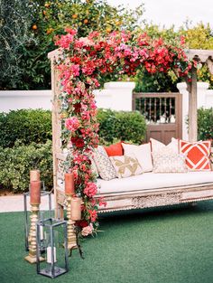 an outdoor seating area with flowers on the arbor and pillows, lanterns, and candles