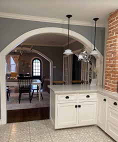 an arched doorway leads into a kitchen with white cabinets and counter tops, along with a dining room table