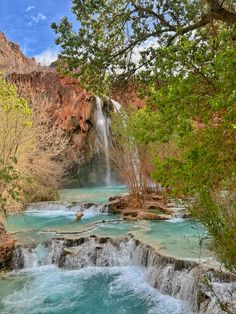 a waterfall in the middle of a river with blue water and trees on both sides