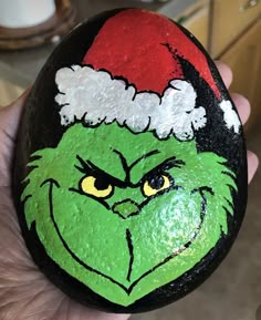a hand painted rock with the grin face on it, wearing a santa claus hat