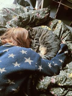 a woman laying in bed next to a cat on top of a blanket with stars