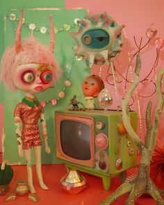 a doll is standing in front of a television set with pink hair and eye makeup