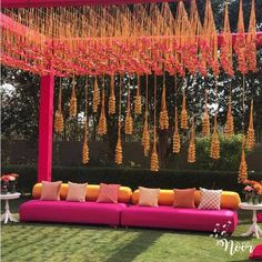 an outdoor seating area with pink couches and orange pillows, hanging flowers and candles