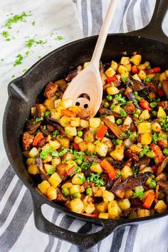 a skillet filled with vegetables and a wooden spoon