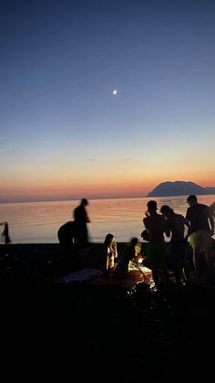 a group of people sitting on top of a beach next to the ocean at sunset