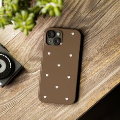 an iphone case with white hearts on it sitting next to a camera and a plant