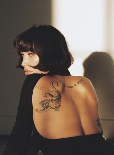 a woman with a dragon tattoo on her back sitting down and looking off to the side