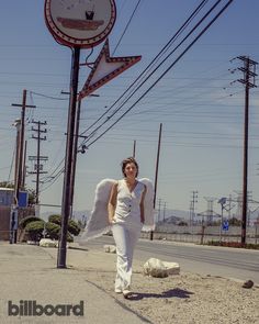 a woman is walking down the street with an angel wings on her back and there are telephone poles in the background