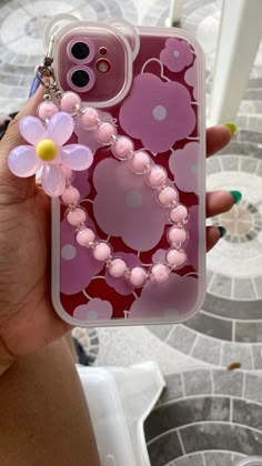 a person holding up a pink phone case with flowers and pearls on the back,