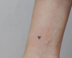 a small black heart tattoo on the wrist