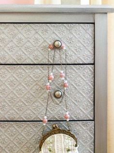 an old dresser has a purse hanging from it's handles and beads on the drawers