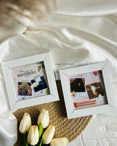 two white framed pictures sitting on top of a bed next to a bouquet of tulips