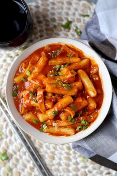 a bowl filled with pasta and sauce on top of a table next to a glass of wine