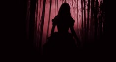 the silhouette of a woman standing in front of tall grass and trees at night with red light