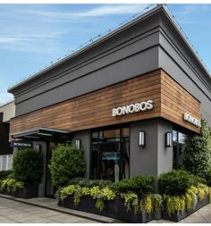 the front of a store with plants and trees in pots on the side of the building