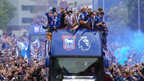 Ipswich Town players on a bus surrounded by thousands of fans