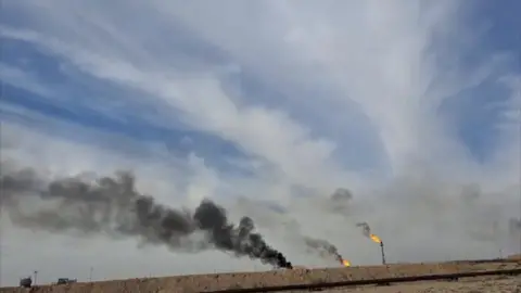 Flaring in Rumaila oil field, black smoke billows and fire from stacks