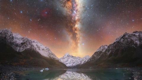 Snowy mountains above a blue lake, with the milky way and stars running down the sky in the centre.