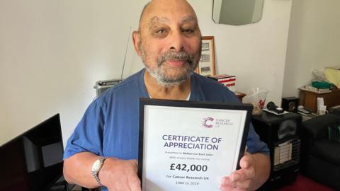 Man holding up a framed certificate showing 42,000 pounds has been raised for Cancer Research UK