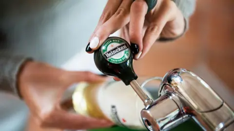 A barperson pours a pint of Heineken lager.