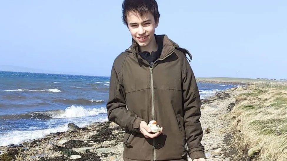 A young teenager holds a plastic duck on a remote beach