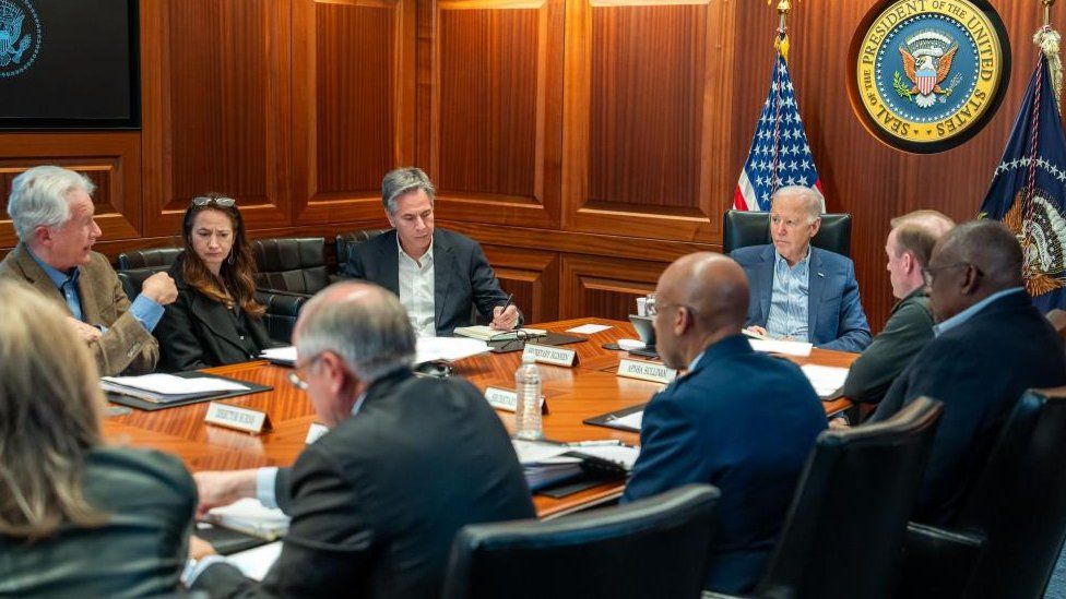 Joe Biden sits at a table and listens to members of the National Security Council